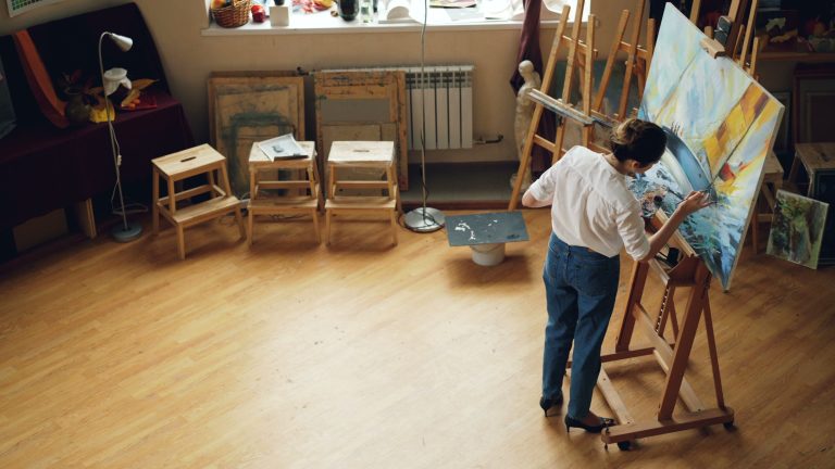 Artist painting on a canvas in a bright studio surrounded by creative supplies
